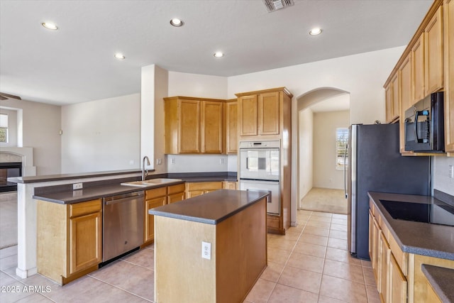 kitchen with a multi sided fireplace, a kitchen island, sink, light tile patterned floors, and black appliances