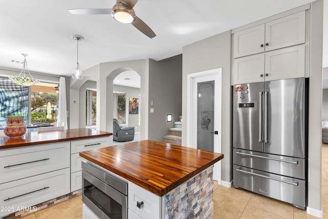 kitchen featuring ceiling fan, light tile patterned floors, arched walkways, appliances with stainless steel finishes, and wooden counters