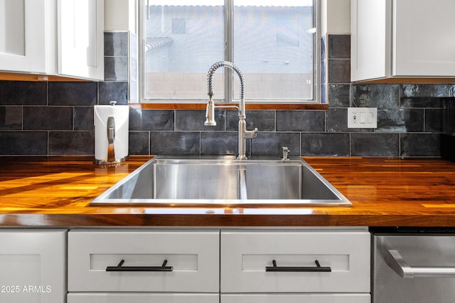 kitchen featuring butcher block counters, white cabinetry, dishwasher, a sink, and decorative backsplash