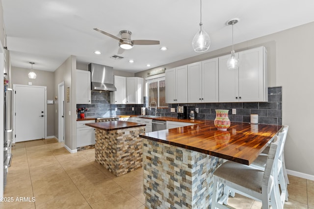 kitchen featuring wall chimney range hood, a ceiling fan, butcher block counters, visible vents, and stainless steel dishwasher