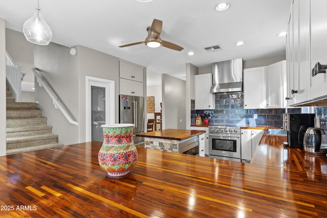 kitchen with ceiling fan, wall chimney exhaust hood, visible vents, wooden counters, and high quality appliances