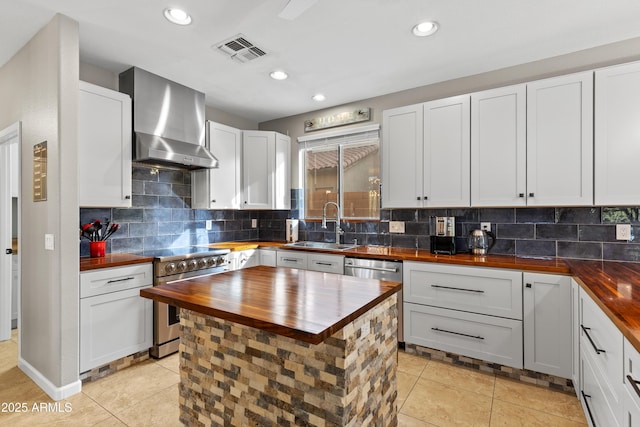 kitchen featuring wall chimney range hood, butcher block counters, visible vents, stainless steel appliances, and a sink
