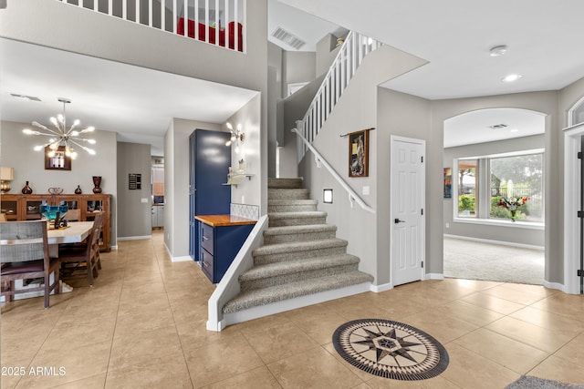 foyer with visible vents, baseboards, arched walkways, a notable chandelier, and stairway