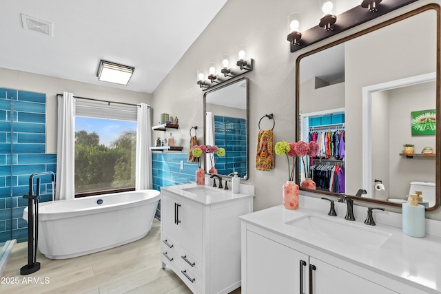 full bathroom with two vanities, visible vents, wood finished floors, a sink, and a freestanding bath