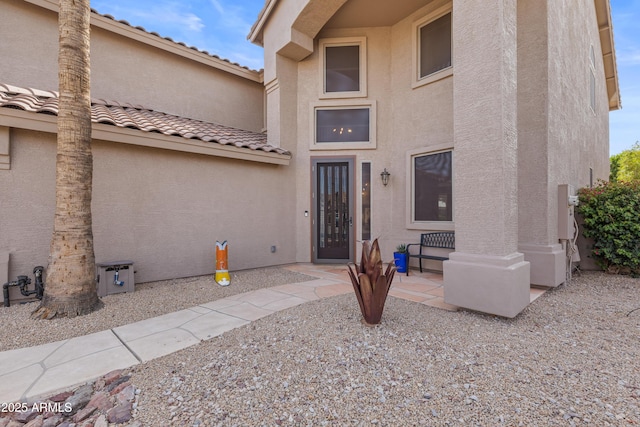view of exterior entry featuring stucco siding and a tiled roof