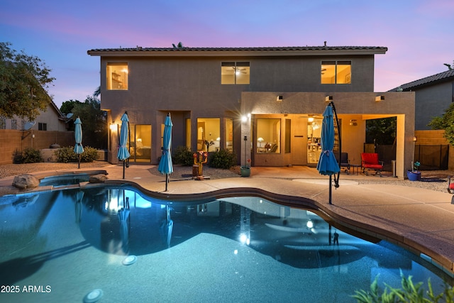 pool at dusk with a patio, a pool with connected hot tub, and fence