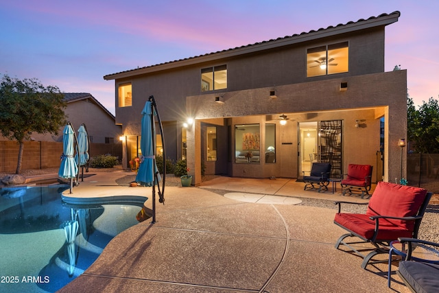 back of property at dusk featuring a patio area, a fenced in pool, fence, and stucco siding