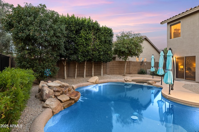 pool at dusk with a patio, a fenced backyard, and a pool with connected hot tub