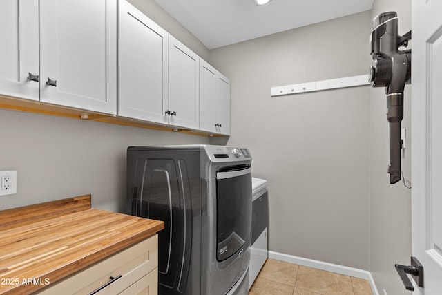 laundry area featuring light tile patterned floors, washer and clothes dryer, baseboards, and cabinet space