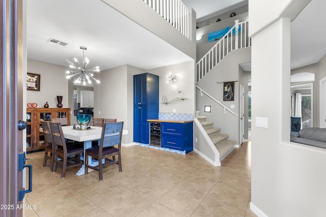 dining space featuring visible vents, stairway, a chandelier, beverage cooler, and baseboards