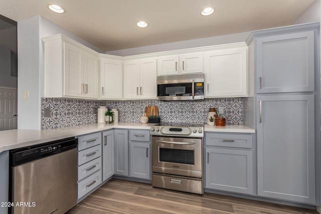 kitchen featuring white cabinets, hardwood / wood-style flooring, tasteful backsplash, gray cabinets, and appliances with stainless steel finishes