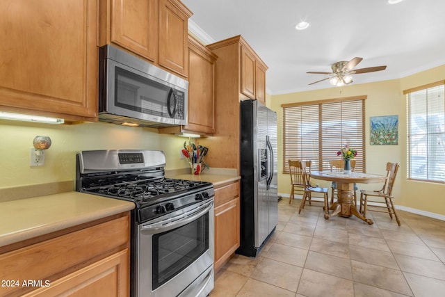 kitchen with appliances with stainless steel finishes, ceiling fan, ornamental molding, and light tile floors