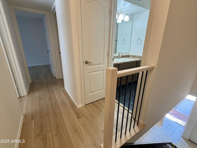 corridor with light wood finished floors, a sink, an upstairs landing, visible vents, and baseboards