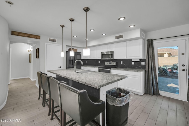 kitchen featuring appliances with stainless steel finishes, a sink, arched walkways, light wood-type flooring, and backsplash