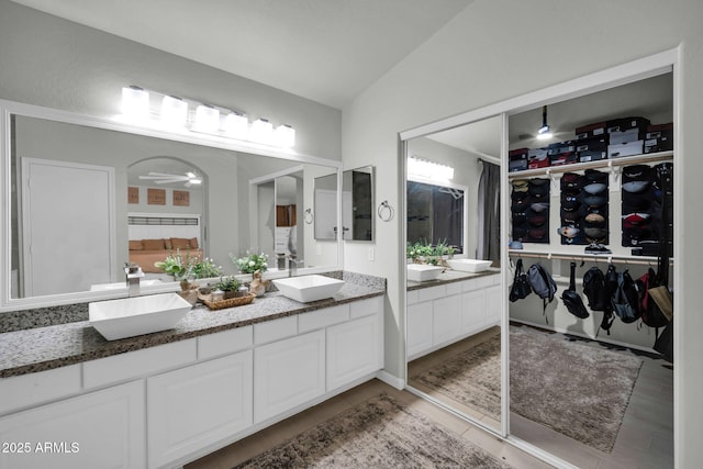 bathroom with double vanity, a walk in closet, vaulted ceiling, wood finished floors, and a sink