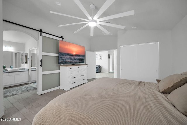 bedroom with a closet, wood finished floors, a barn door, connected bathroom, and arched walkways