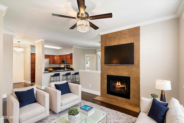 living area featuring crown molding, baseboards, dark wood finished floors, a ceiling fan, and a tile fireplace
