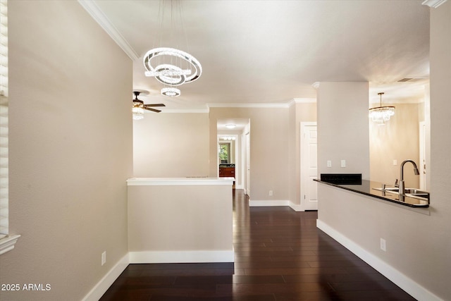 interior space featuring a sink, dark wood-type flooring, baseboards, ceiling fan with notable chandelier, and ornamental molding