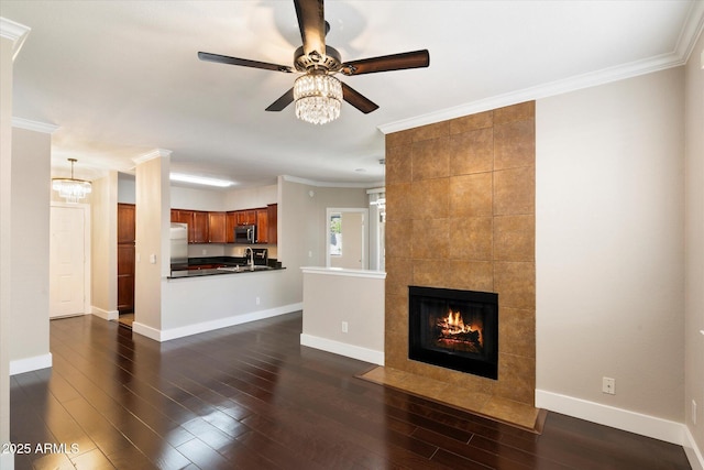 unfurnished living room featuring crown molding, baseboards, ceiling fan, a tiled fireplace, and dark wood-type flooring
