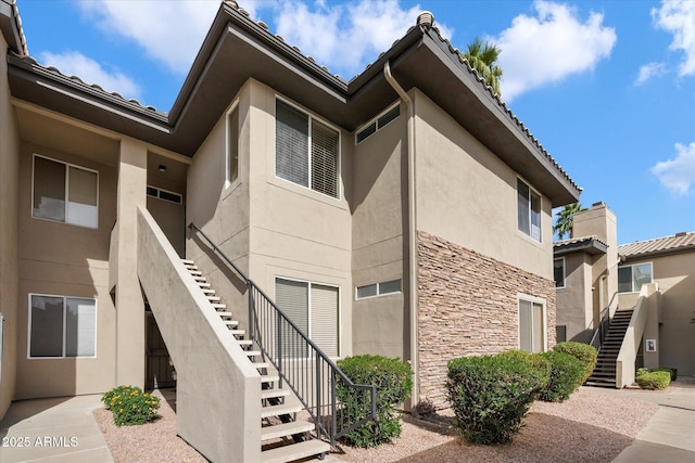 exterior space with stairs, stucco siding, and stone siding