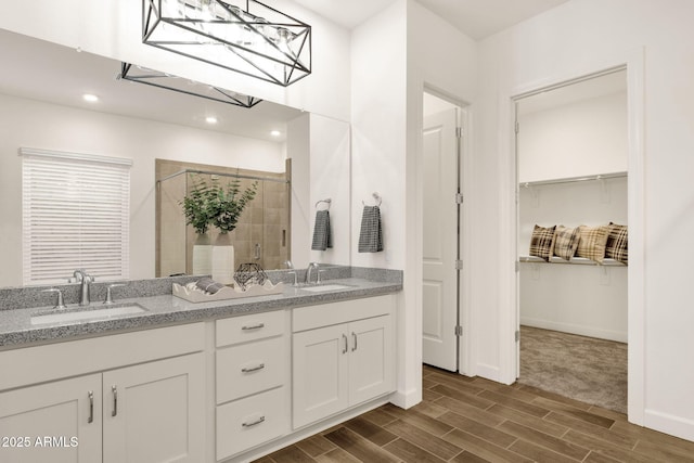 bathroom featuring a shower stall, a walk in closet, a sink, and wood finish floors