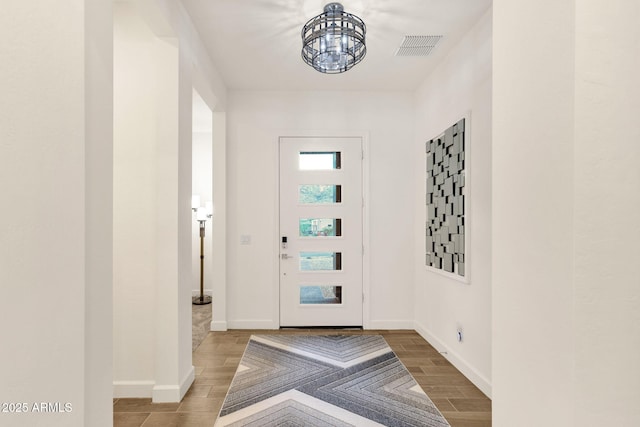 foyer entrance featuring wood tiled floor, visible vents, a notable chandelier, and baseboards