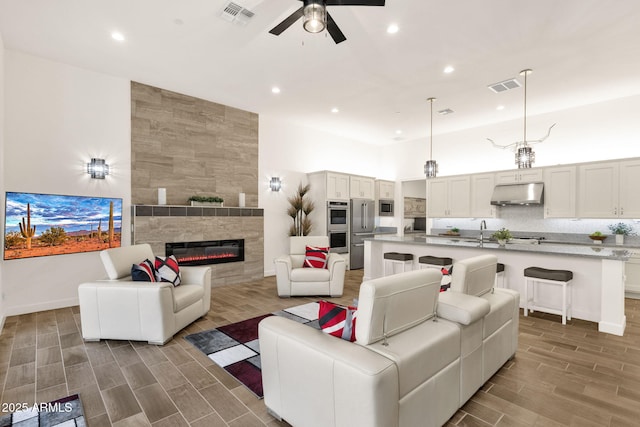 living area featuring a ceiling fan, wood tiled floor, visible vents, and a tiled fireplace