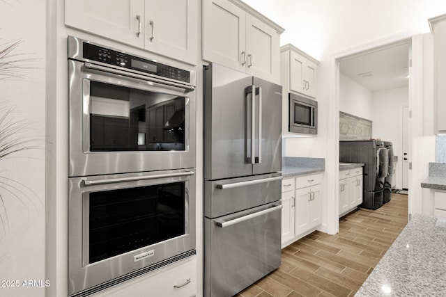 kitchen with white cabinetry, appliances with stainless steel finishes, light stone counters, and wood finish floors