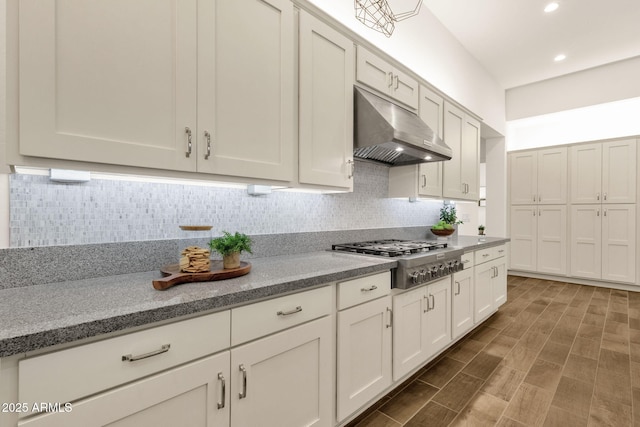 kitchen featuring recessed lighting, stainless steel gas cooktop, under cabinet range hood, backsplash, and light stone countertops