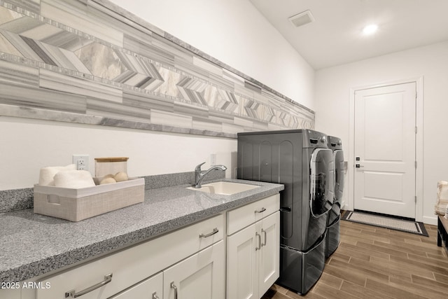 washroom featuring cabinet space, visible vents, washing machine and clothes dryer, wood finish floors, and a sink