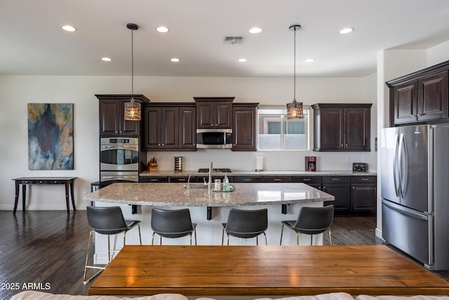 7432 W Bronco Trl, Peoria, AZ 85383 - kitchen featuring stainless steel appliances, a kitchen island with sink, dark brown cabinets, dark wood-style floors, and a breakfast bar area