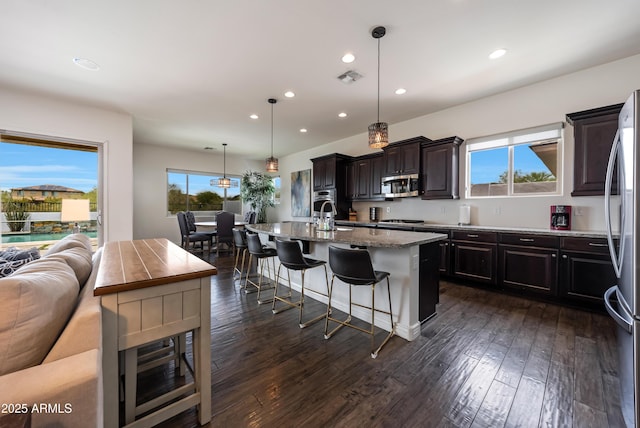 7432 W Bronco Trl, Peoria, AZ 85383 - kitchen featuring appliances with stainless steel finishes, recessed lighting, a breakfast bar area, a kitchen island with sink, and light stone counters