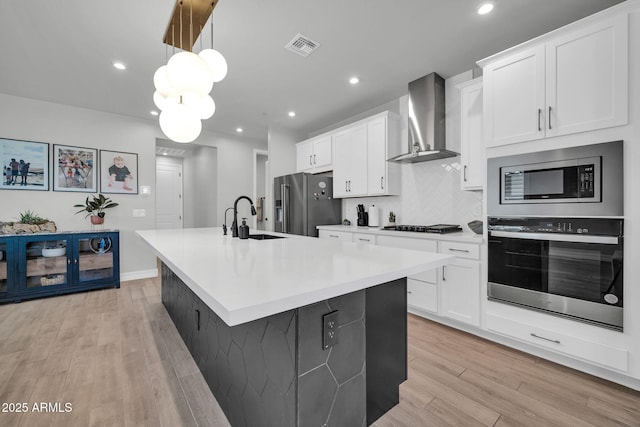 31435 N 130th Ave, Peoria, AZ 85383 - kitchen with a kitchen island with sink, a sink, light wood-style floors, wall chimney range hood, and appliances with stainless steel finishes