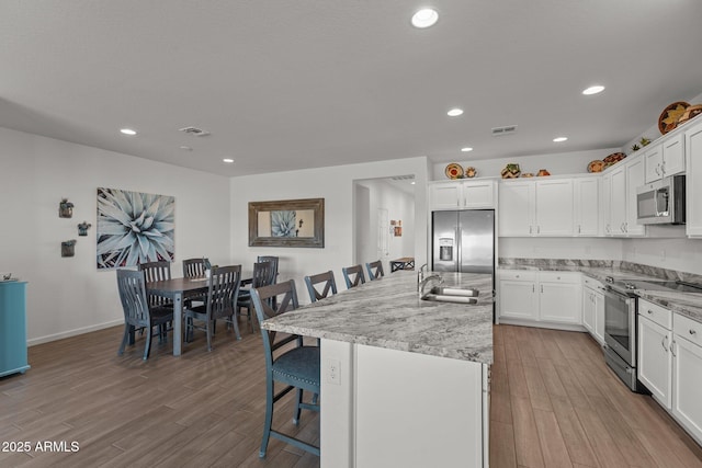 kitchen featuring stainless steel appliances, a kitchen island with sink, a breakfast bar, and white cabinetry