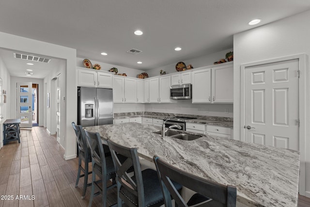 kitchen featuring a center island with sink, white cabinets, a breakfast bar, and appliances with stainless steel finishes