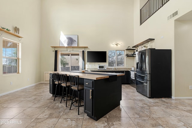 kitchen with visible vents, open shelves, a center island, stainless steel fridge, and dark cabinets