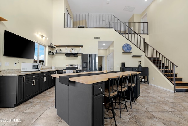 kitchen featuring baseboards, visible vents, stainless steel appliances, a kitchen breakfast bar, and dark cabinets