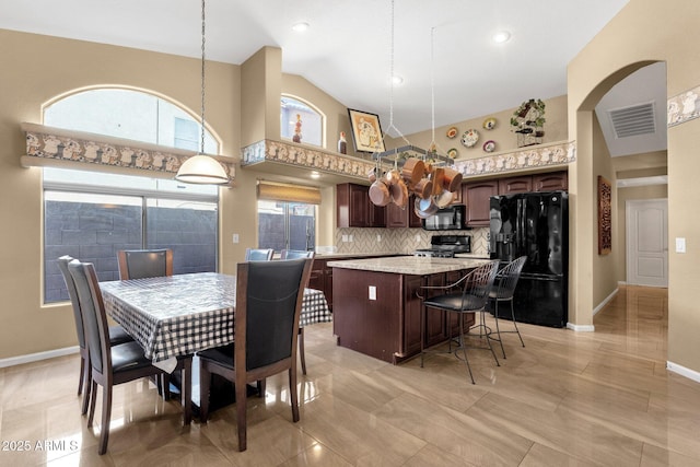 kitchen featuring black appliances, a kitchen island, dark brown cabinetry, a kitchen bar, and decorative backsplash