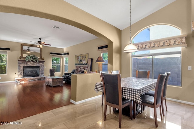 dining space with a fireplace, arched walkways, ceiling fan, and baseboards