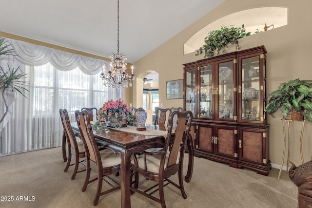 dining space featuring light carpet, arched walkways, lofted ceiling, and a chandelier