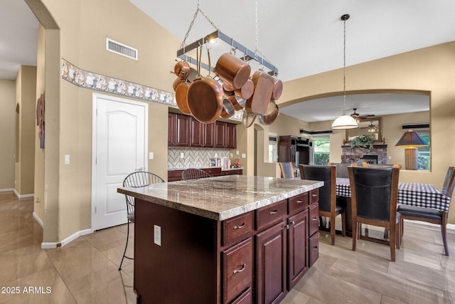 kitchen featuring arched walkways, baseboards, a kitchen island, a towering ceiling, and a stone fireplace