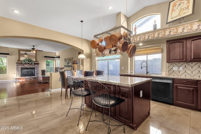 kitchen featuring dishwasher, a sink, a ceiling fan, a center island, and light stone countertops