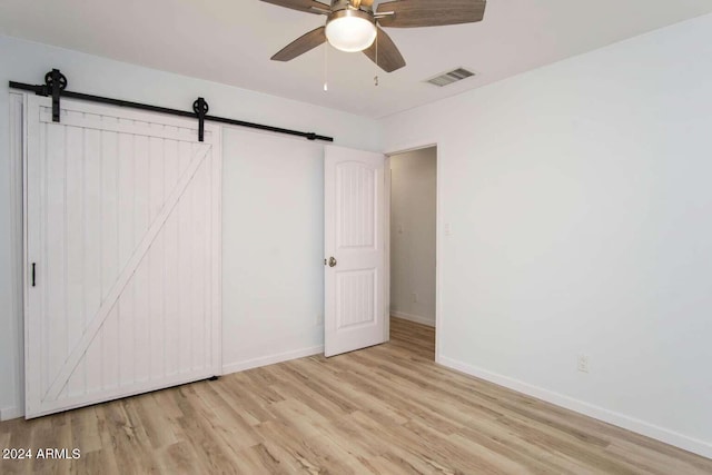 unfurnished bedroom featuring light wood-type flooring, ceiling fan, and a barn door