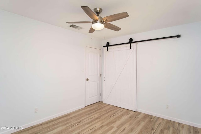 unfurnished bedroom featuring light hardwood / wood-style floors, ceiling fan, and a barn door