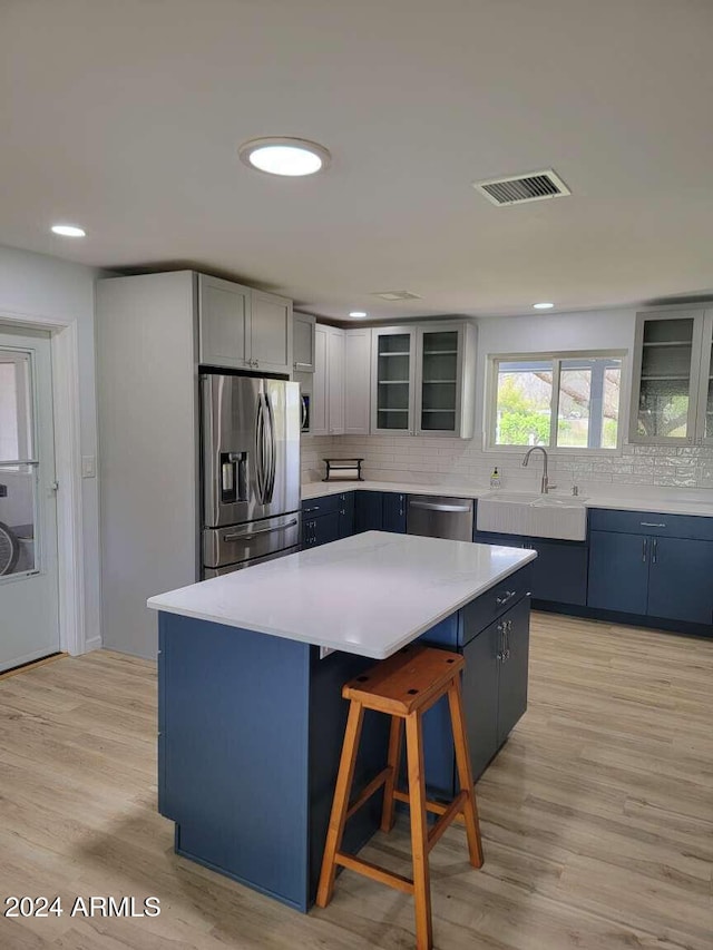 kitchen featuring light wood-type flooring, sink, a kitchen island, stainless steel appliances, and backsplash