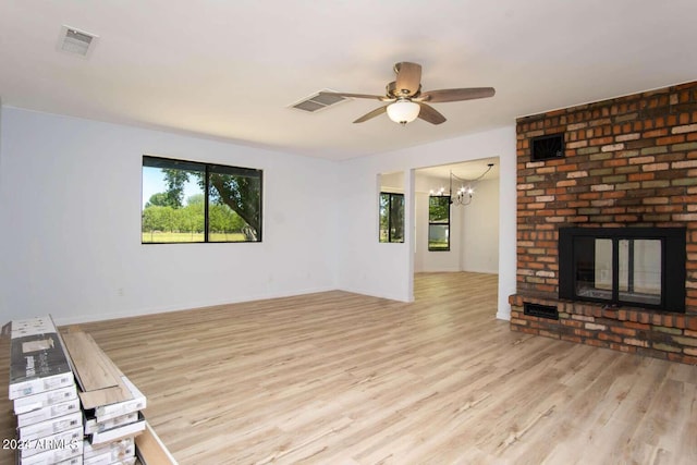 unfurnished living room featuring a brick fireplace, ceiling fan with notable chandelier, and light hardwood / wood-style floors