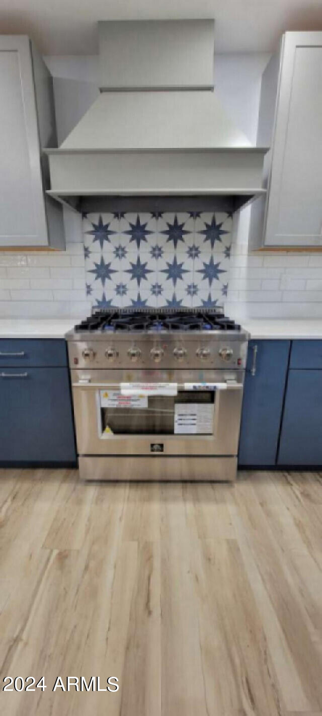 kitchen featuring decorative backsplash, white cabinets, high end stainless steel range oven, and light hardwood / wood-style floors