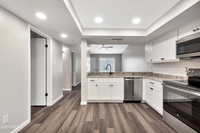 kitchen with appliances with stainless steel finishes, sink, white cabinets, light stone counters, and dark hardwood / wood-style floors