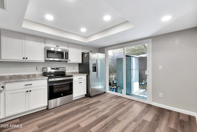 kitchen featuring a tray ceiling, white cabinets, appliances with stainless steel finishes, and light hardwood / wood-style floors