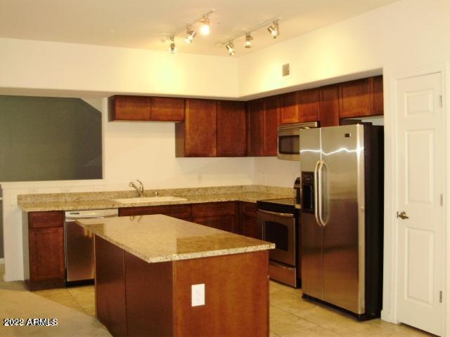 kitchen with light stone counters, light tile patterned floors, a kitchen island, a sink, and stainless steel appliances